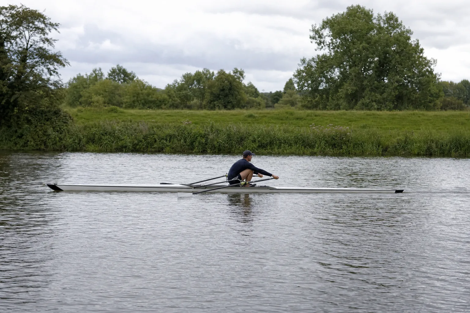 A single sculler at the catch, compressed at the front of the slide with shins vertical, arms straight and both blades dropping into the water