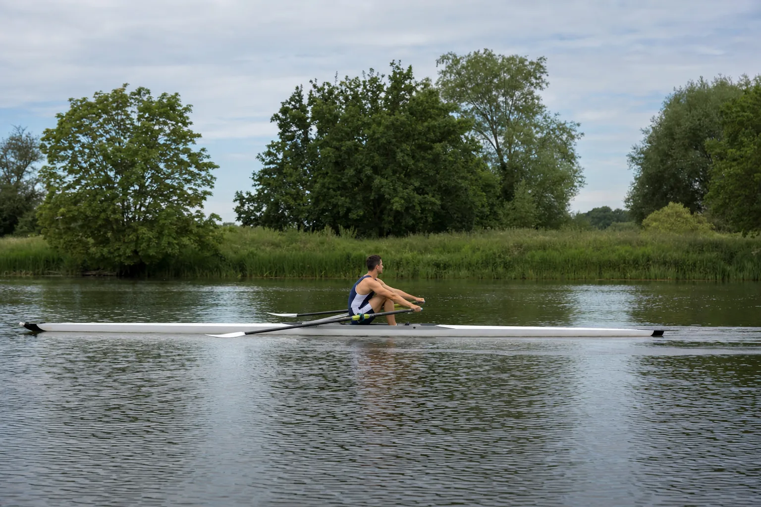 A single sculler on the recovery, arms extended away and body pivoted forward, with both blades turned flat and skimming just above the water