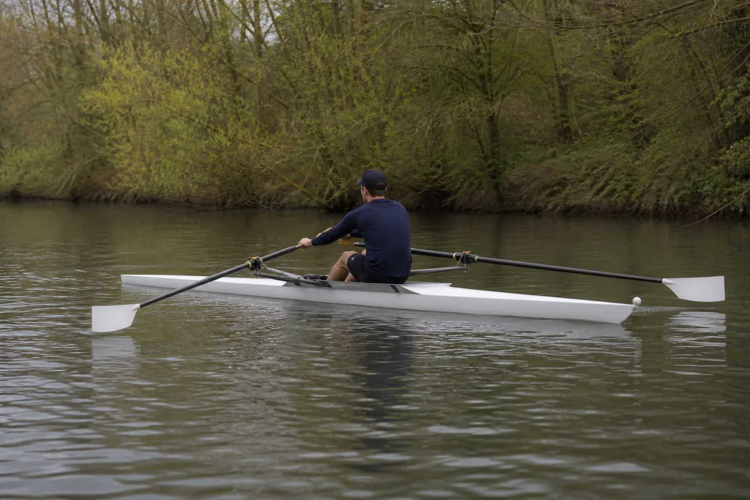 A single sculler mid-stroke, holding one oar in each hand, with the tapered shafts, the grips and the asymmetric blades all clearly visible